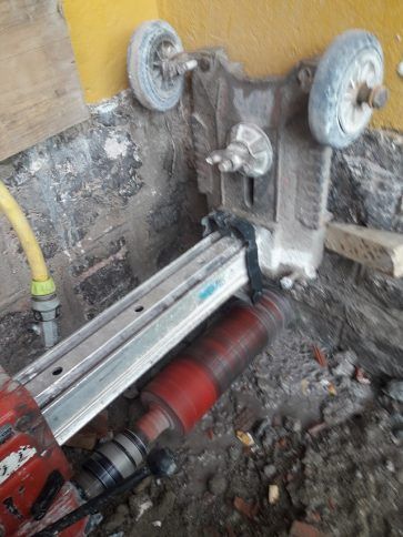 Una máquina de construcción perfora un piso de concreto cerca de una pared, con componentes rojos y plateados expuestos.
