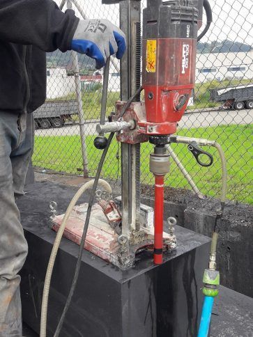 Un trabajador utiliza un taladro de núcleo rojo en una caja de servicios públicos de hormigón al aire libre.