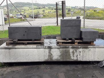 Bloques de hormigón negro sobre palés de madera encima de una plataforma de hormigón cerca de una valla.