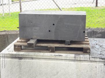 Bloque de hormigón gris sobre un palé de madera encima de una plataforma de hormigón.