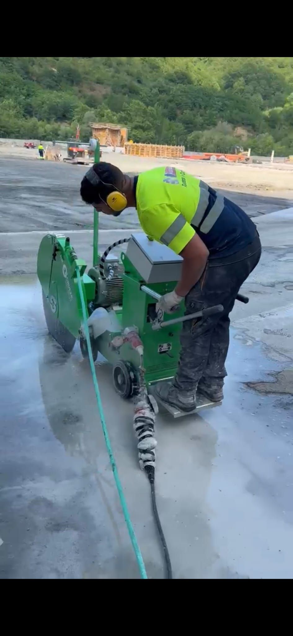Obrero utilizando una sierra para hormigón verde en una obra de construcción al aire libre húmeda.