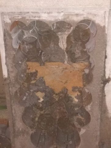 Pared dañada con una gran mancha de yeso marrón expuesto rodeada de pintura gris agrietada.