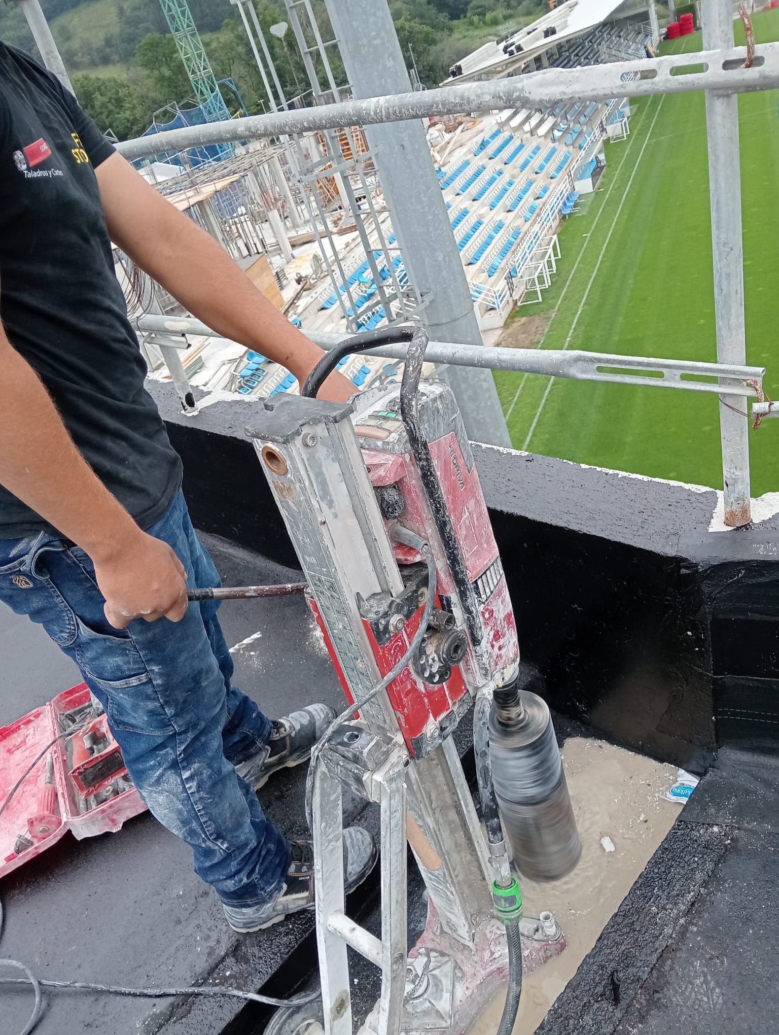 Un trabajador se encuentra en una plataforma del estadio, junto a una barandilla roja, con vistas a las gradas verdes que hay debajo.