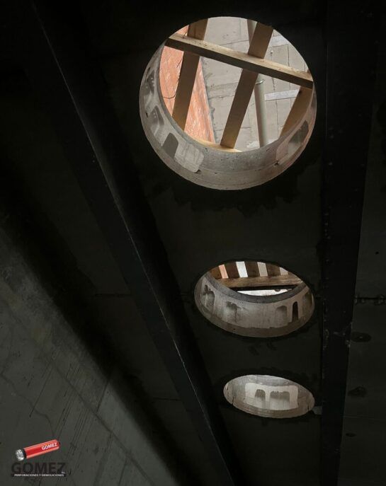 Tres claraboyas redondas en un techo oscuro, que dejan ver vigas de madera y estructuras de ladrillo en la parte superior.