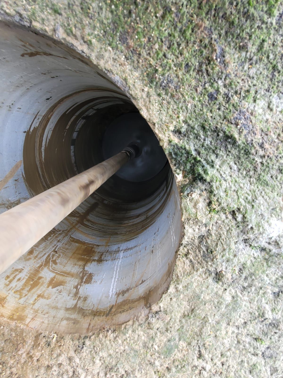 Abertura de un tubo de metal oxidado en la hierba con un poste de madera insertado en su interior.