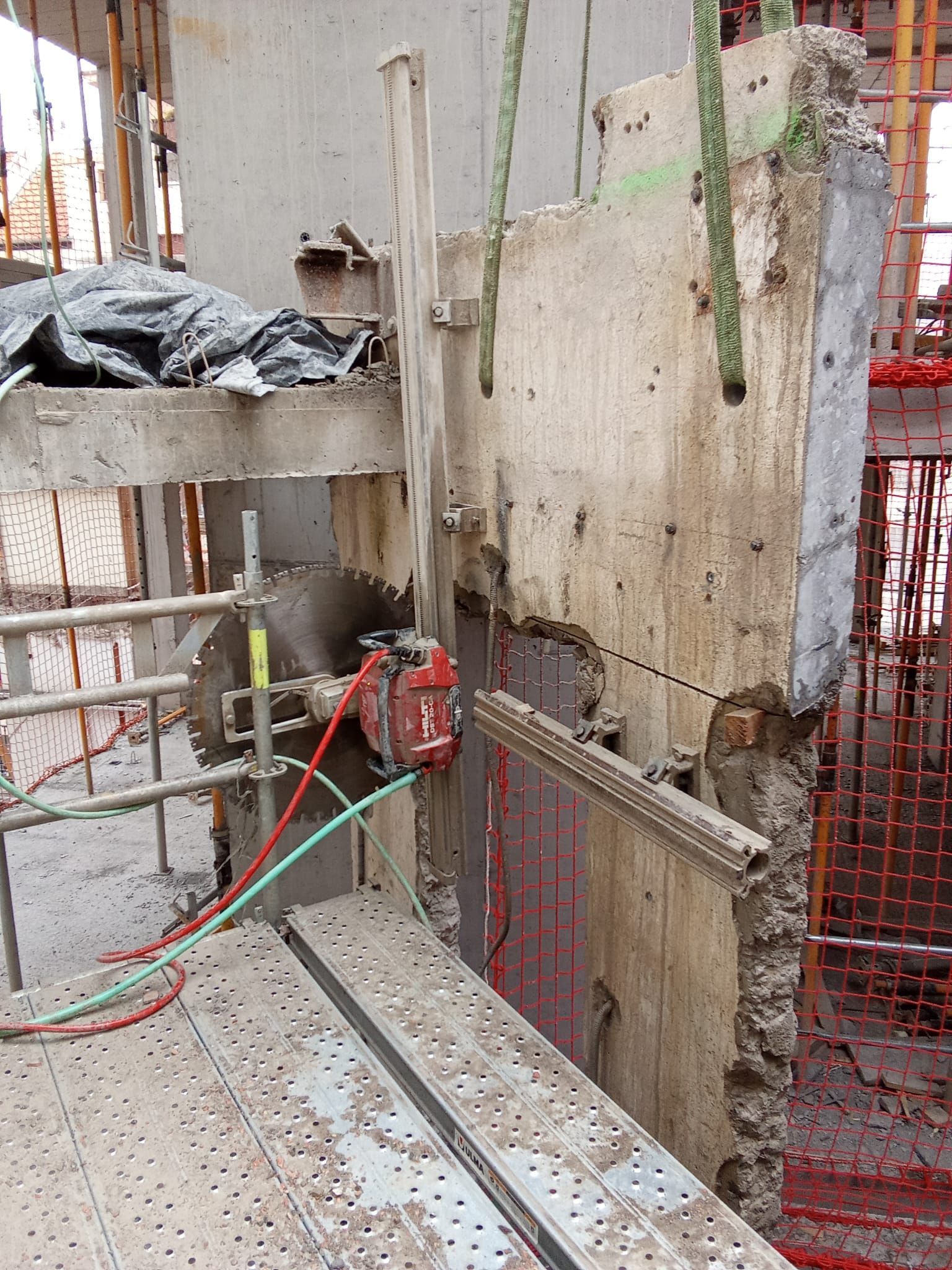 Obra en construcción con paneles de pared de hormigón, andamios y equipos rojos sobre una plataforma mojada.