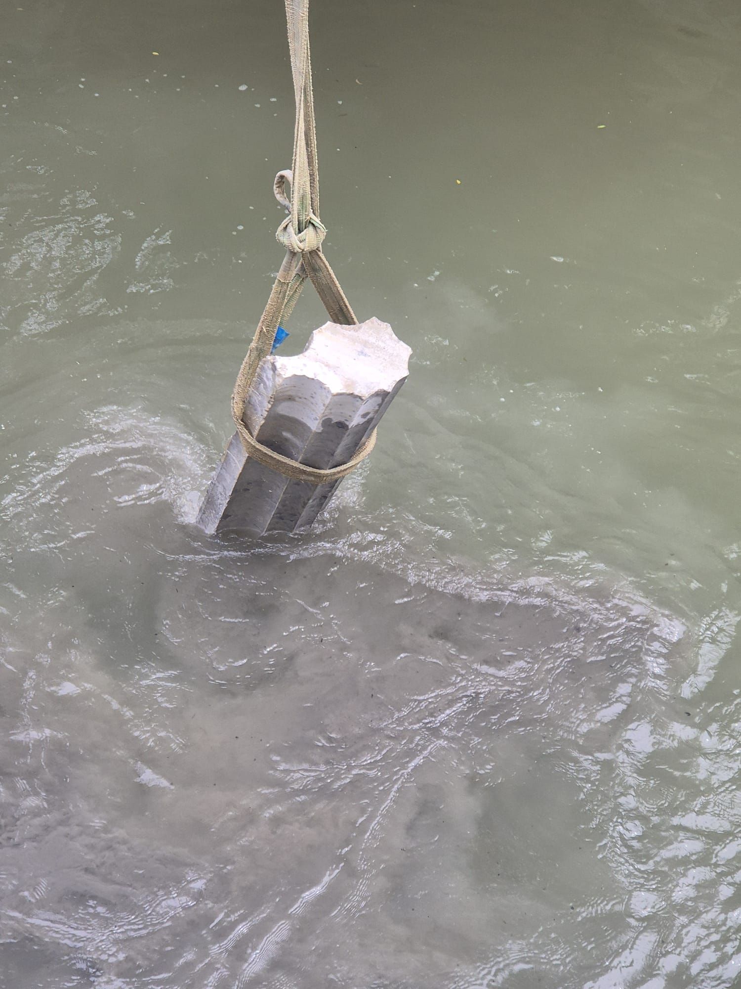 Un objeto cilíndrico negro colgando de una cuerda en agua turbia, parcialmente sumergido y salpicando.