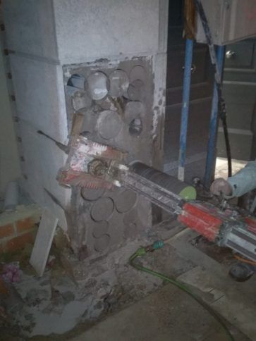 Taladro de construcción cortando una pared de hormigón alrededor de tuberías de servicios expuestas en un área.