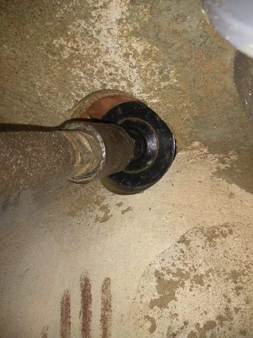 Primer plano de una tubería metálica que entra en una pared de hormigón rugoso a través de una junta de goma negra.
