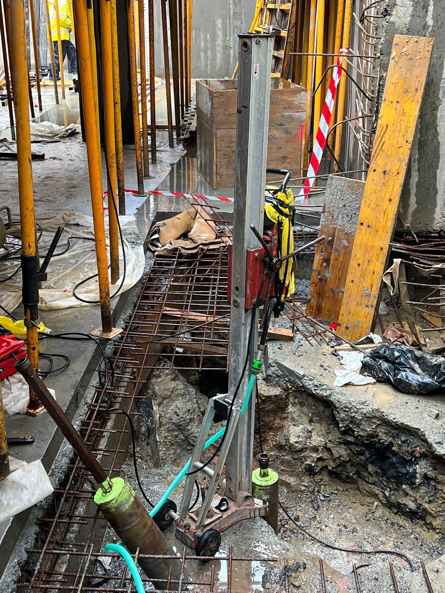 Zanja de construcción con barras de refuerzo, agua turbia y soportes verticales de hormigón en reparación.