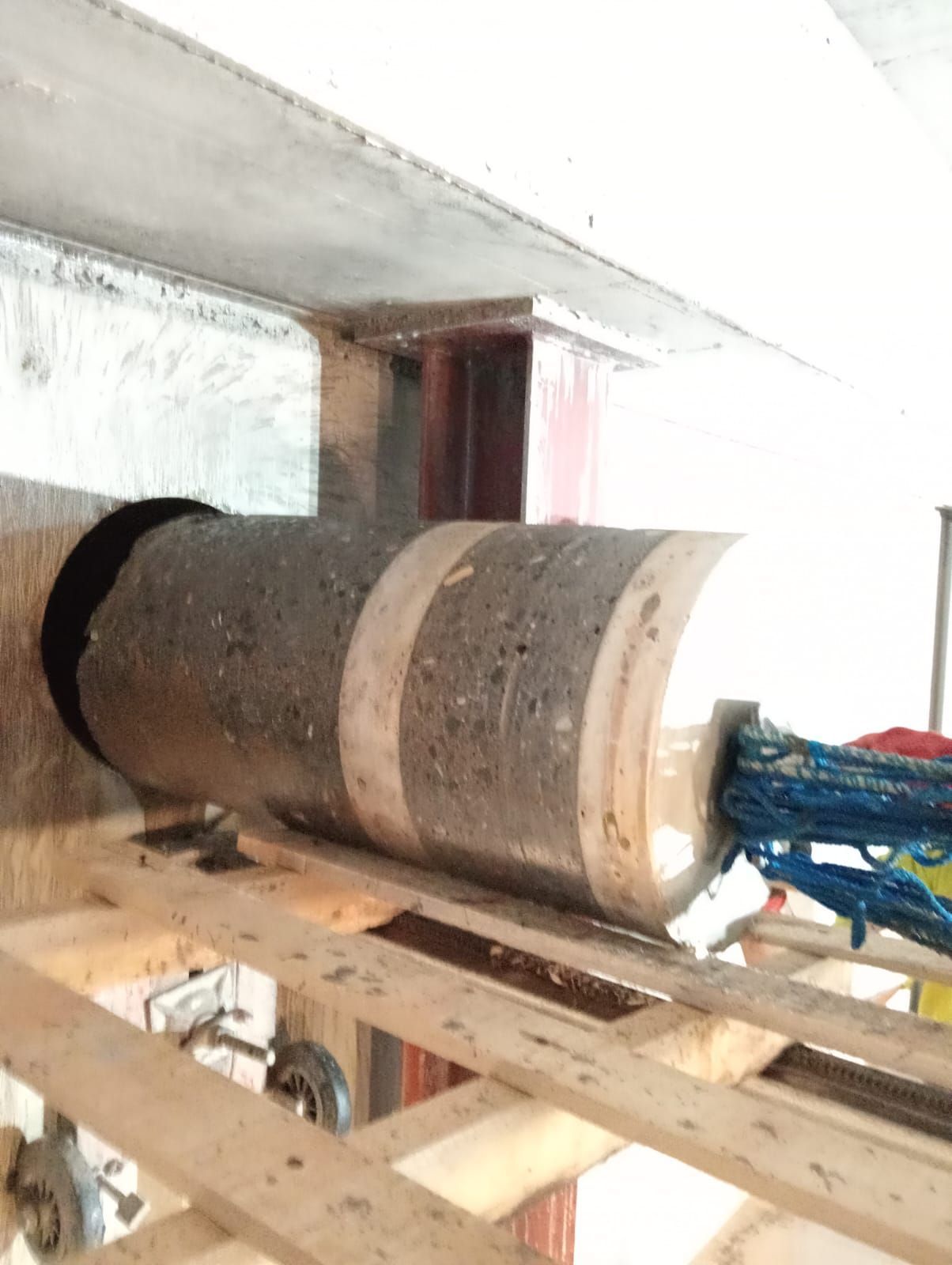 Gran rodillo cilíndrico sobre maquinaria en una sala industrial, con componentes rojos y azules.