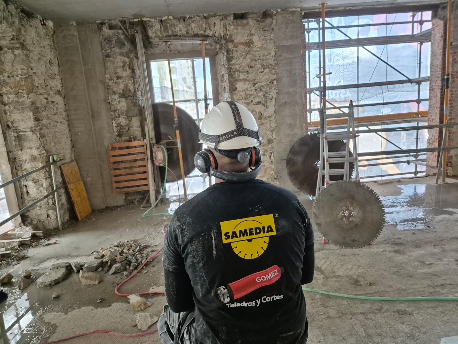 Un trabajador con casco se encuentra en una habitación polvorienta y sin terminar, rodeada de andamios y materiales de construcción.