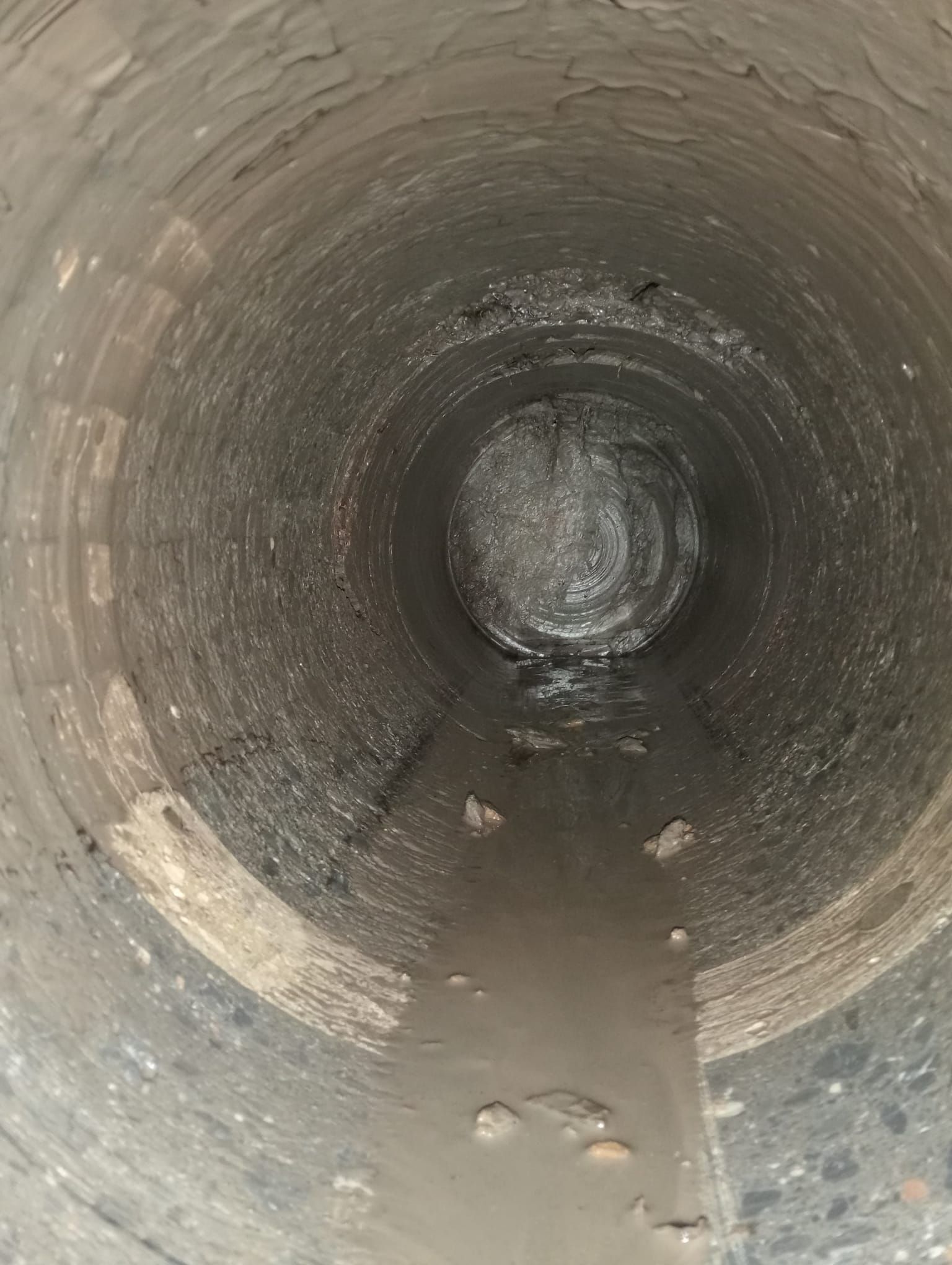 Dentro de una estrecha tubería o túnel de hormigón con agua poco profunda y escombros en el suelo.