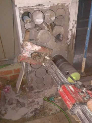 Muro dañado con agujeros circulares de mampostería expuestos y escombros, con herramientas.