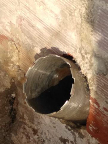 Primer plano de una tubería de metal que sobresale de una superficie de pared rugosa y manchada.