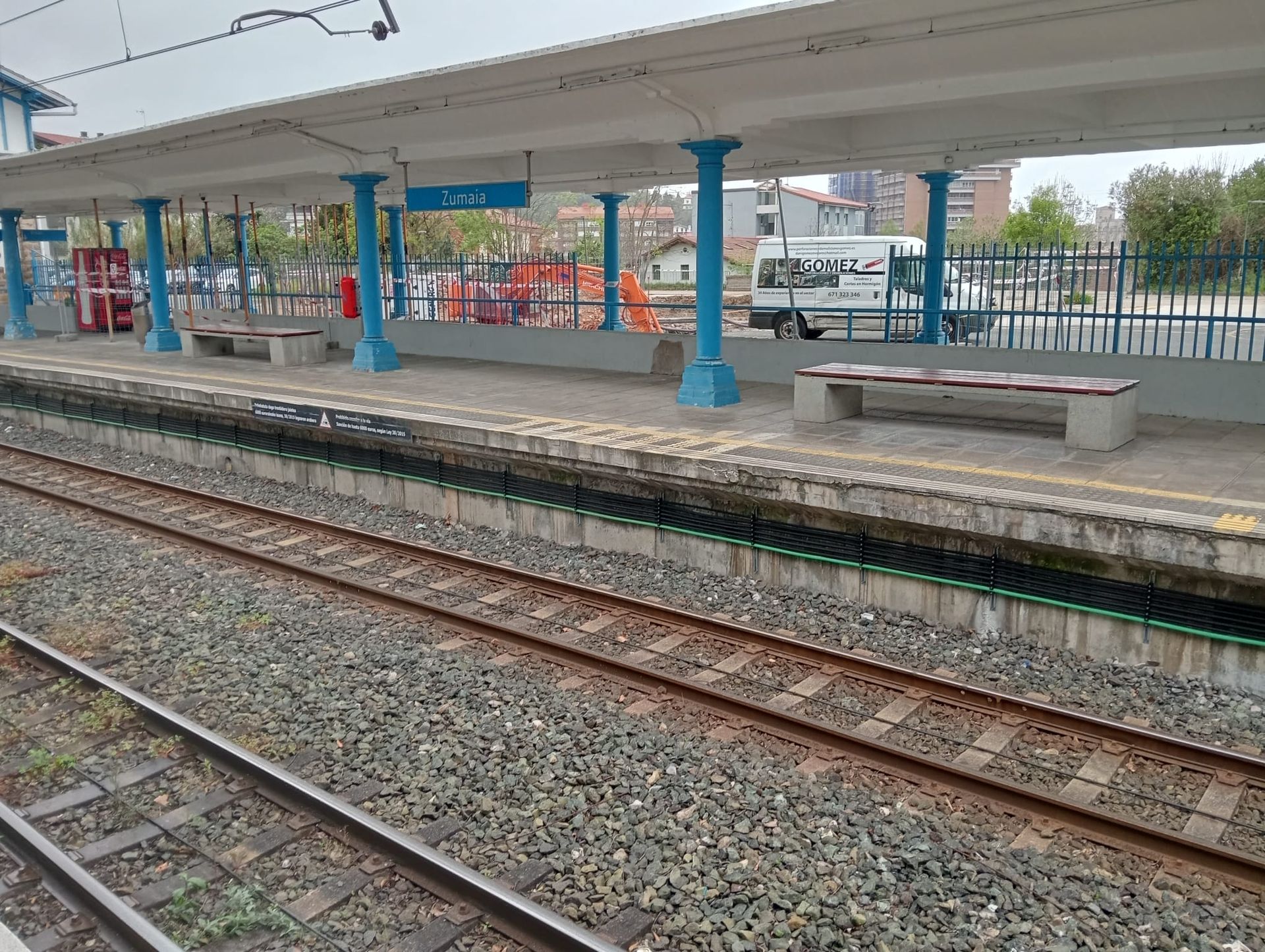 Andén vacío de una estación de tren junto a varias vías férreas, bajo una marquesina con columnas de soporte azules.