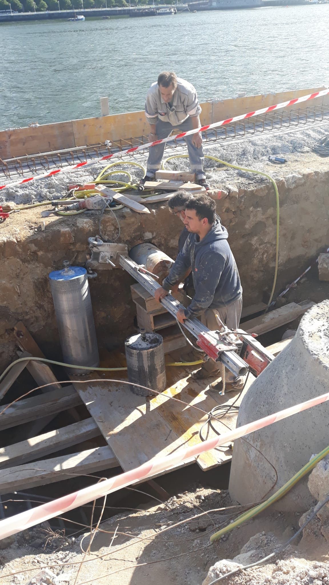 Obreros reparando la ladera de la ribera de un río, rodeados de herramientas y materiales de construcción.
