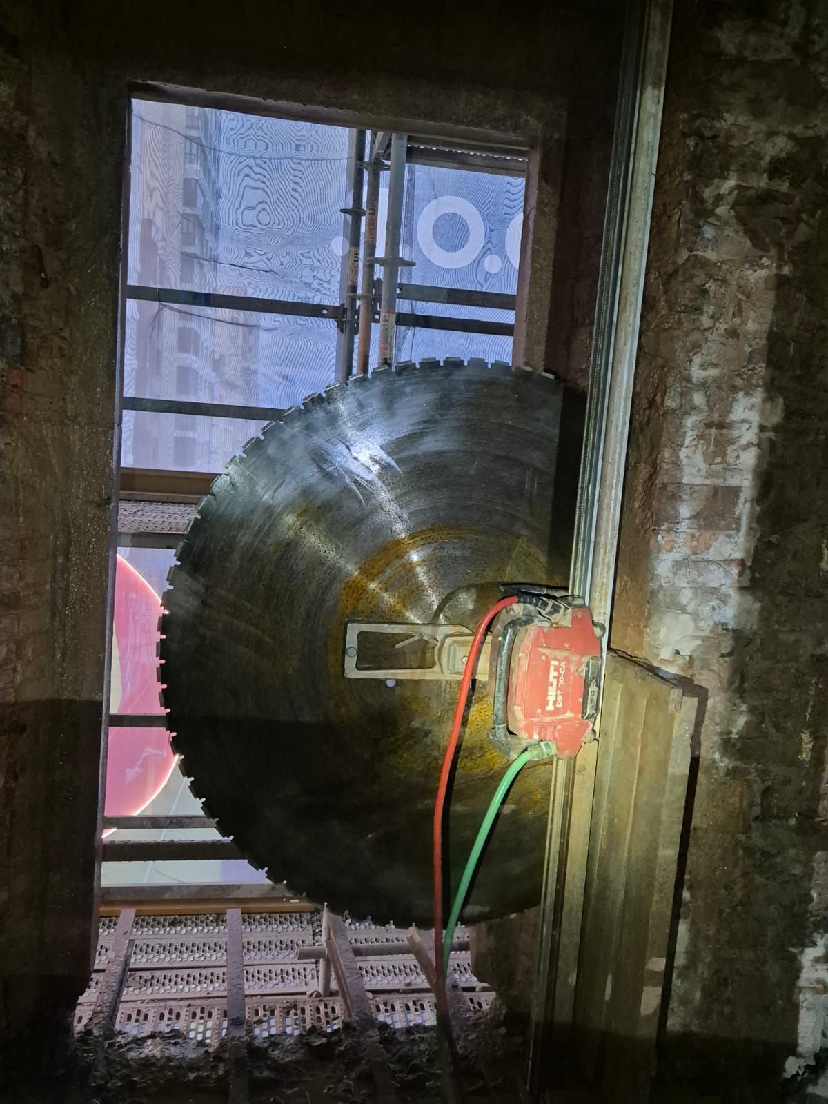 Gran carrete o rueda negra montada en una ventana desgastada, con cables rojos y verdes conectados.