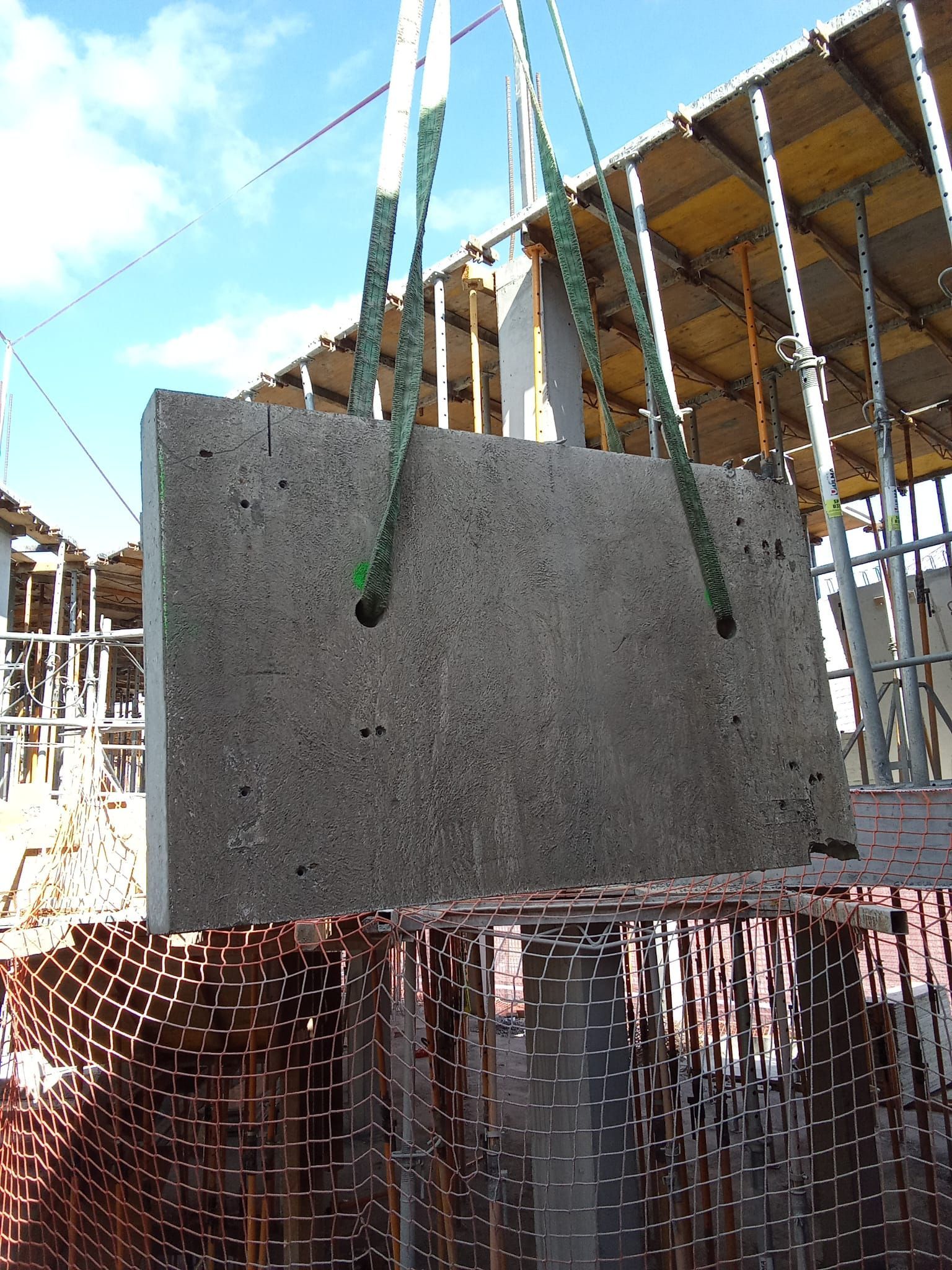 En una obra en construcción, se está levantando un panel de pared de hormigón con la ayuda de correas verdes.