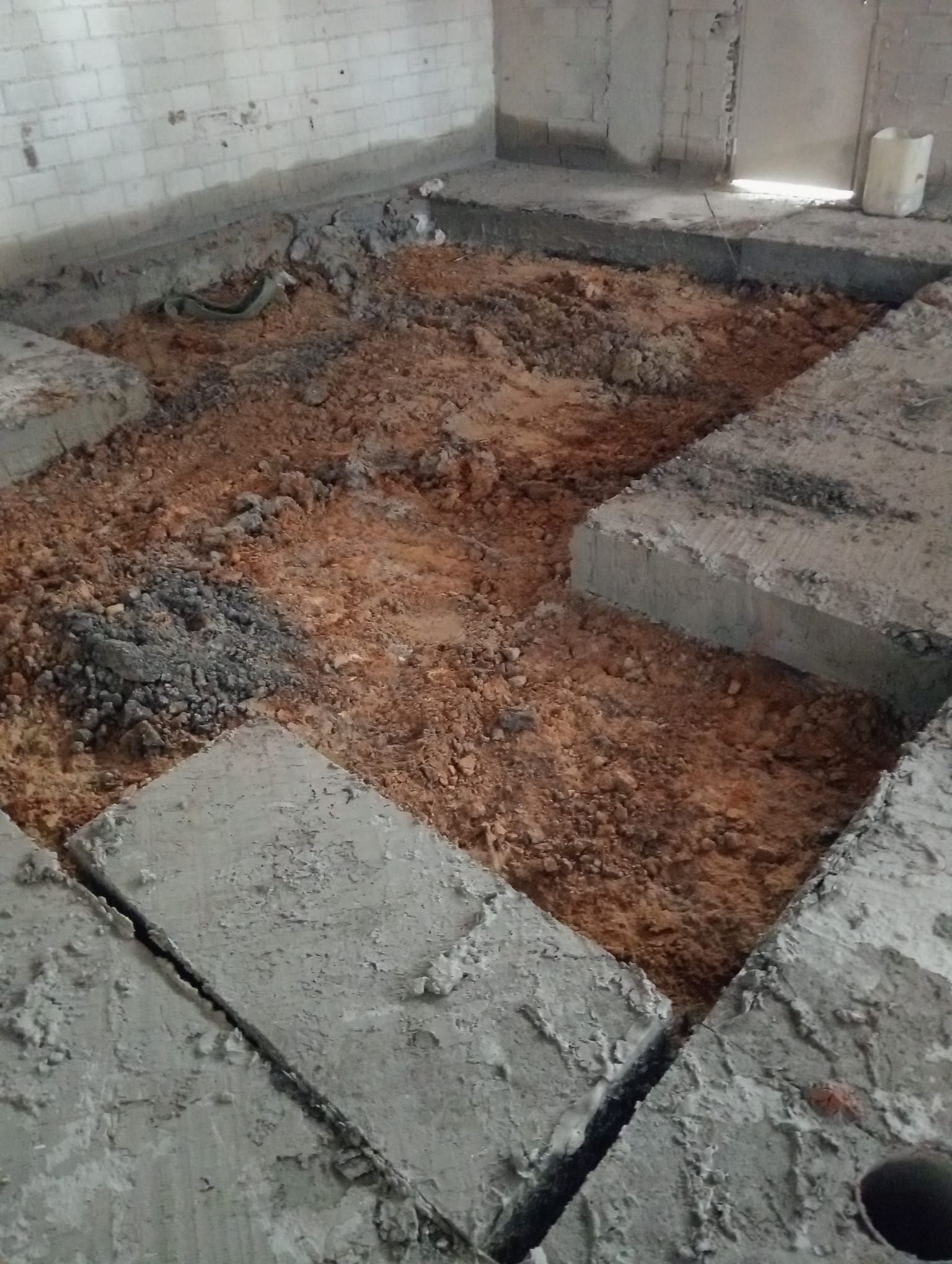 Se observa el suelo de los cimientos al descubierto, con tierra, zapatas de hormigón y un agujero en una habitación sin terminar.