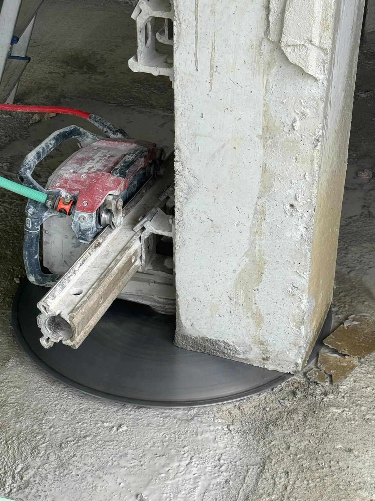 Cortando hormigón con una sierra a través de un piso alrededor de una columna de soporte vertical.