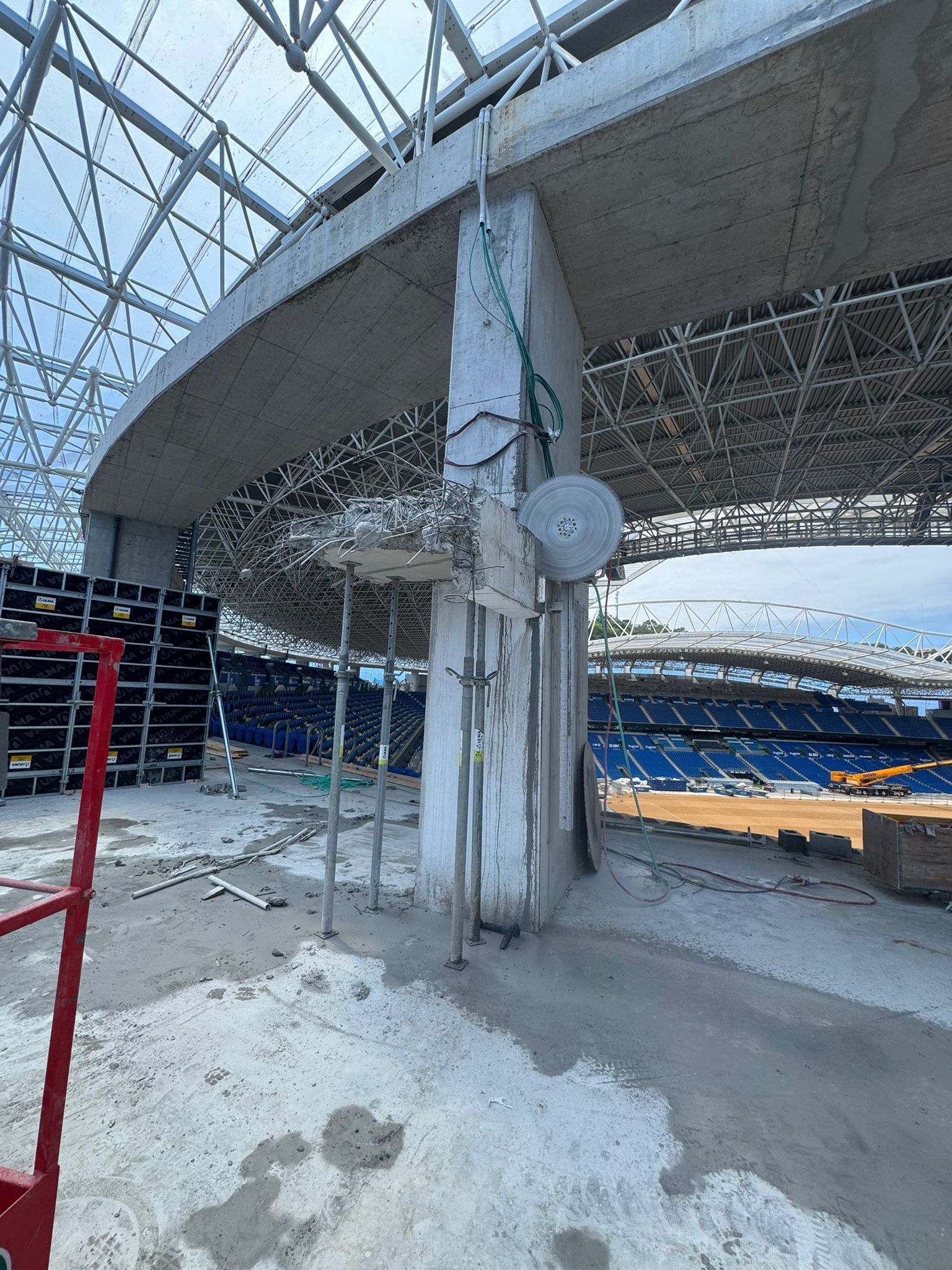 Interior del estadio cubierto de nieve con redes dañadas, soportes de hormigón y asientos azules bajo un techo curvo.