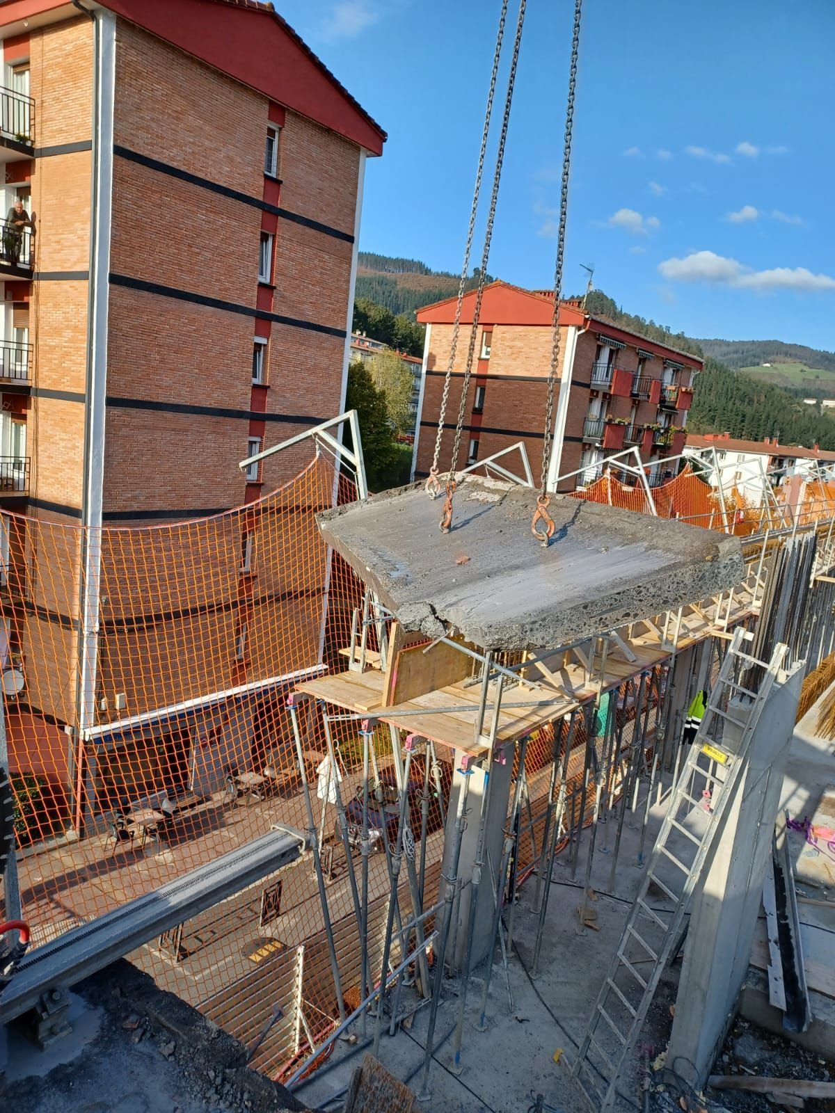 Obra en construcción con edificios de apartamentos de ladrillo rojo, andamios y encofrados de hormigón bajo un cielo despejado.