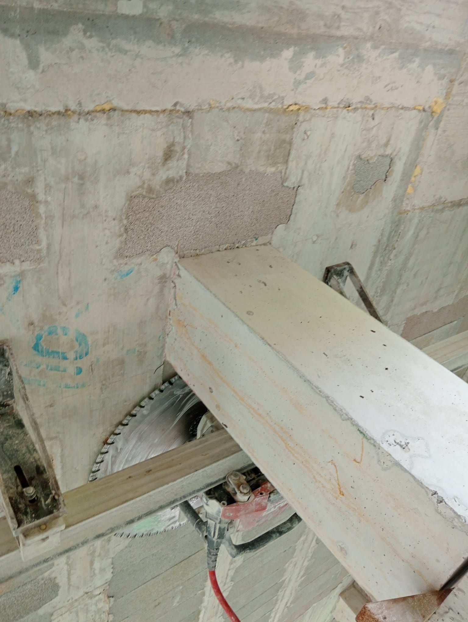 Zona de construcción con una gran viga blanca frente a un muro de hormigón visto y maquinaria expuesta en la parte inferior.
