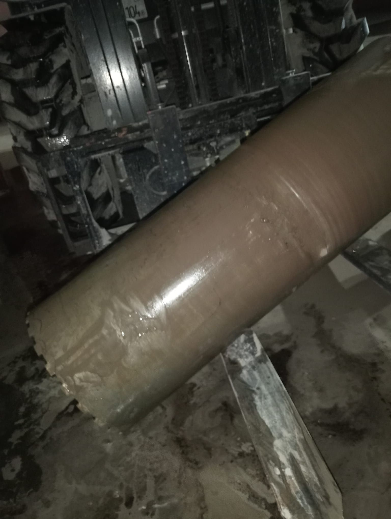 Gran tubo cilíndrico marrón sobre maquinaria en un entorno industrial con poca luz.