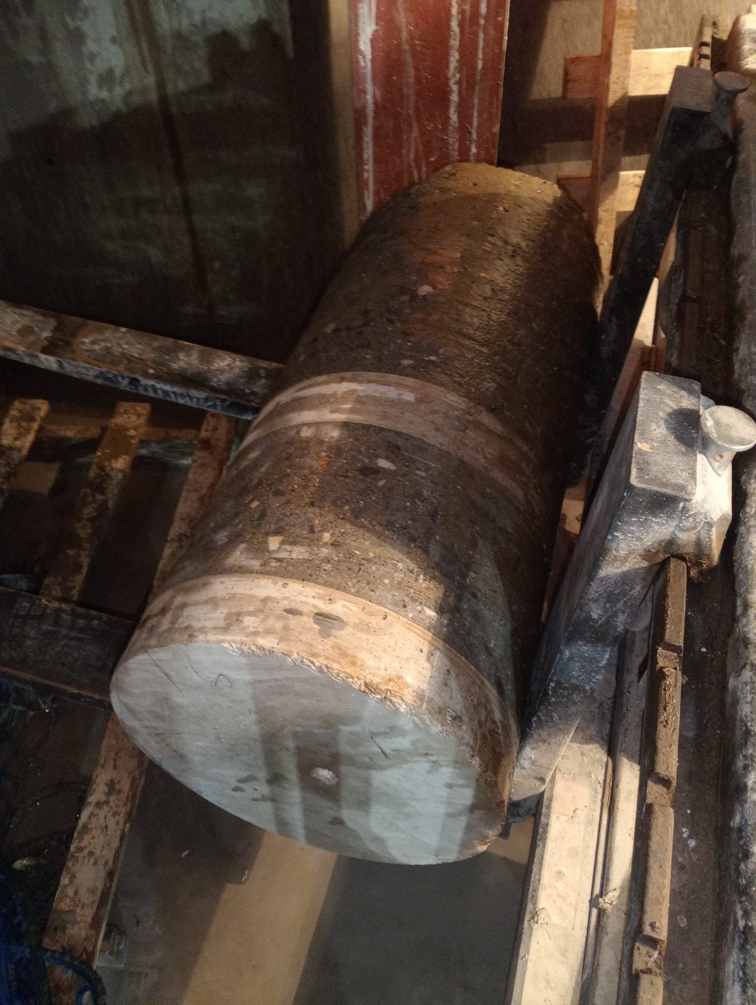 Primer plano de un gran cilindro metálico en una máquina industrial desgastada, cubierto de óxido y suciedad.