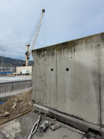 Muro de hormigón en una obra en construcción con una grúa y cielo nublado al fondo.