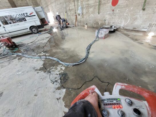 Obra en construcción donde los trabajadores alisan el hormigón fresco con una allanadora mecánica y mangueras.