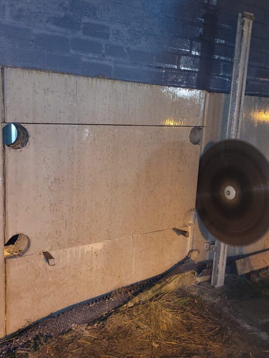 Muro azul y beige junto a una carretera mojada por la noche, con un objeto circular borroso en primer plano.