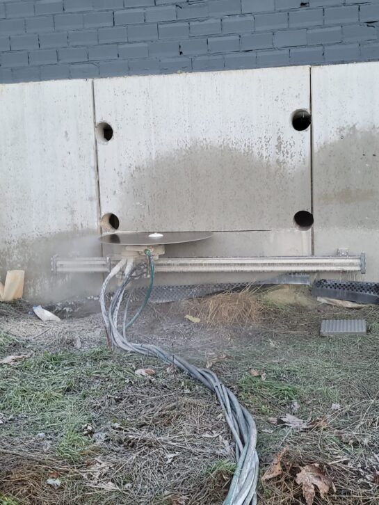 Cables de servicios públicos dañados tirados en el suelo junto a una pared exterior blanca con agujeros de montaje.