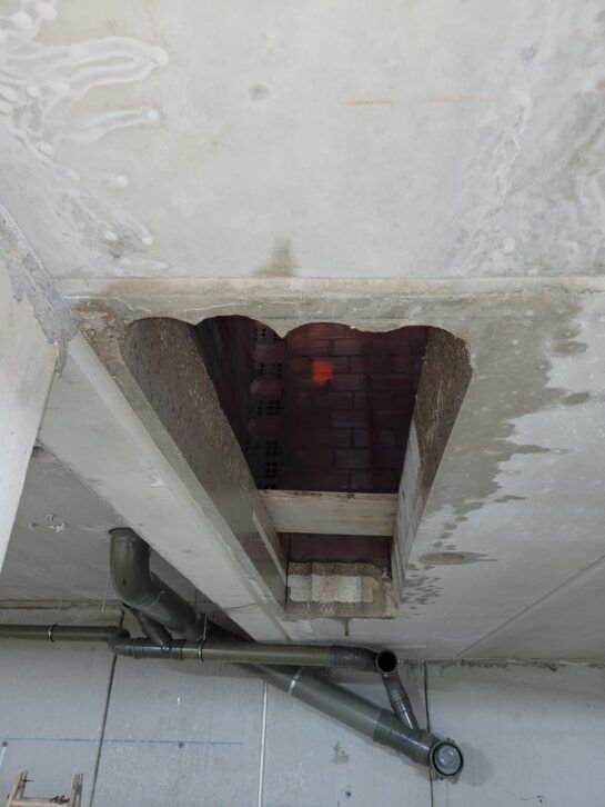 Abertura en el techo dañada con tuberías expuestas y una luz roja visible en el interior.