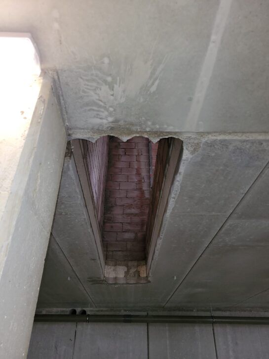 Techo dañado con una abertura rectangular que deja al descubierto el ladrillo y el aislamiento en un espacio interior.