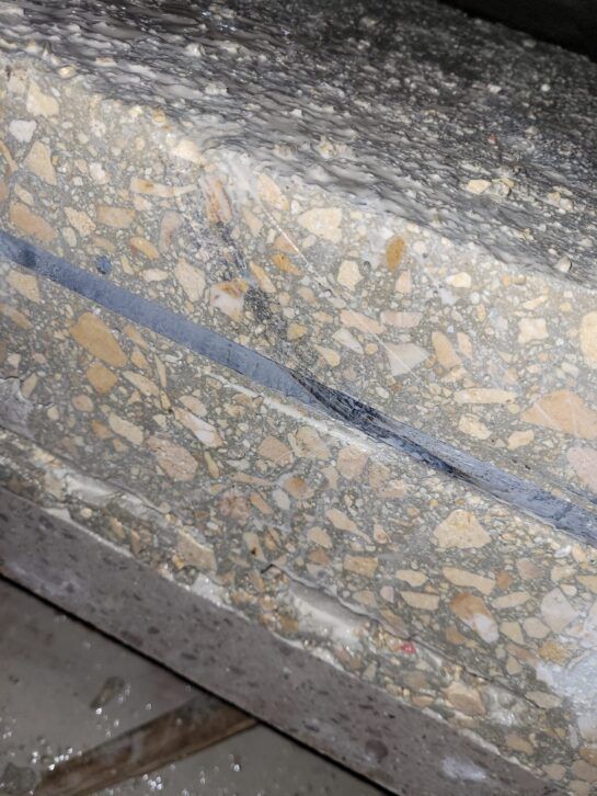 Primer plano de un escalón de hormigón gris moteado con una franja azul y un borde metálico.