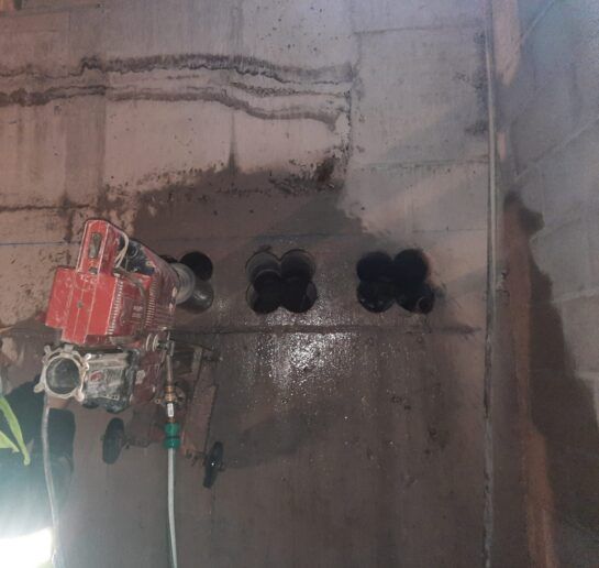 Una perforadora roja corta agujeros circulares en una pared de hormigón dentro de una obra en construcción.