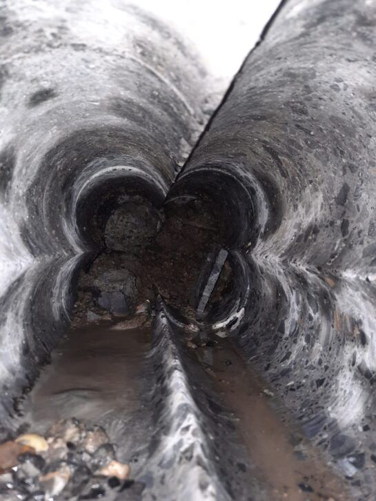 Primer plano del interior de un túnel o tubería estrecha y fangosa, con agua acumulada en el fondo.