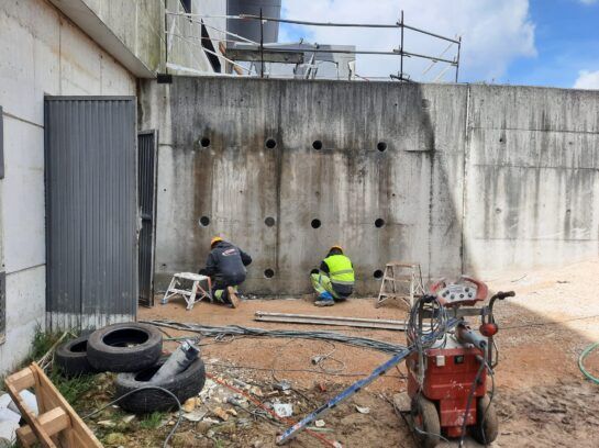 Trabajadores reparando un muro de contención de hormigón en una obra de construcción, con herramientas.