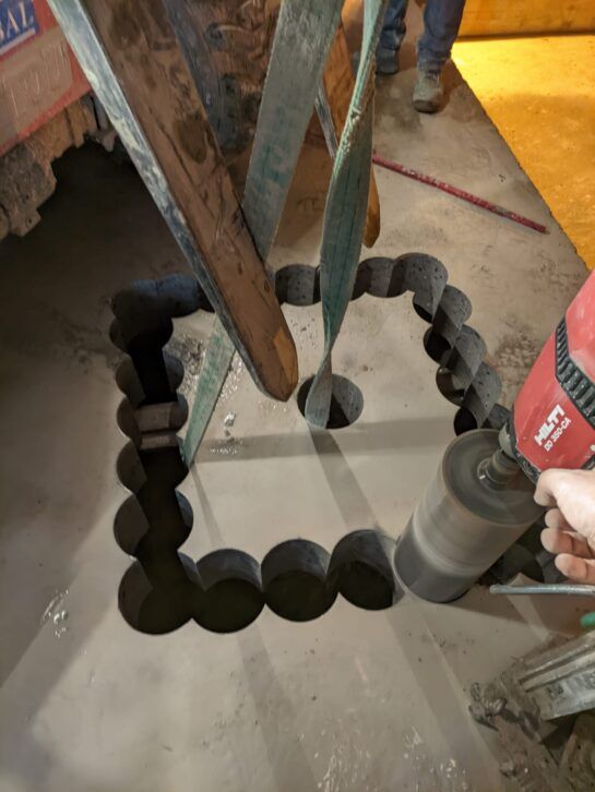 Un trabajador taladra un agujero cuadrado en el suelo de hormigón de una obra en construcción.