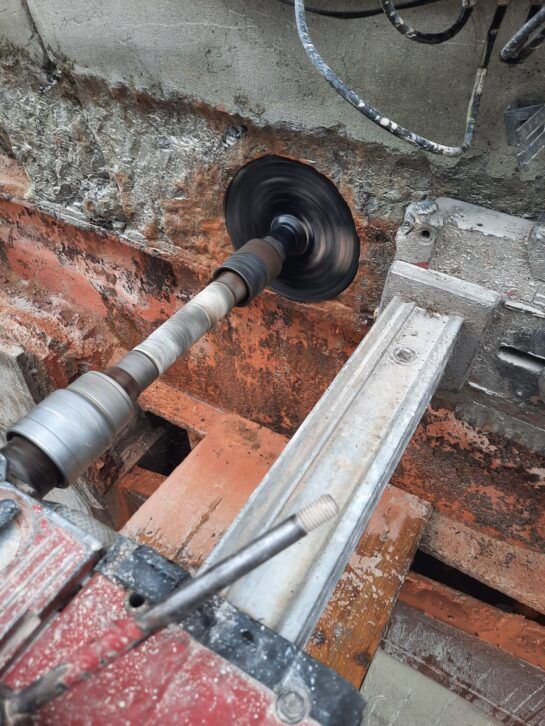 Sierra de corte de pared cortando hormigón en una zona de construcción en mal estado con ladrillos expuestos y polvo.