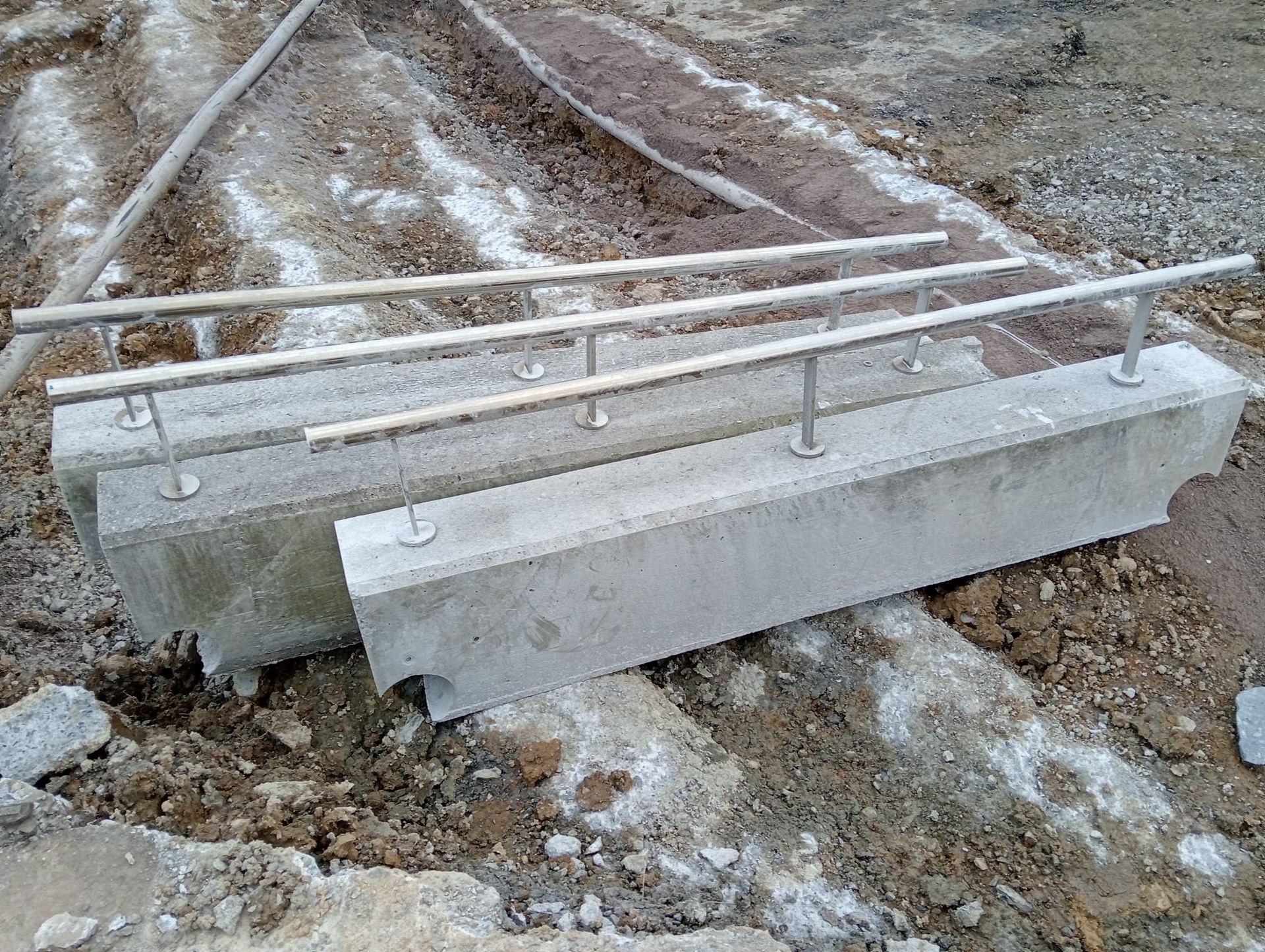 Barreras de hormigón con barandillas metálicas en una obra en construcción embarrada y cubierta de nieve.