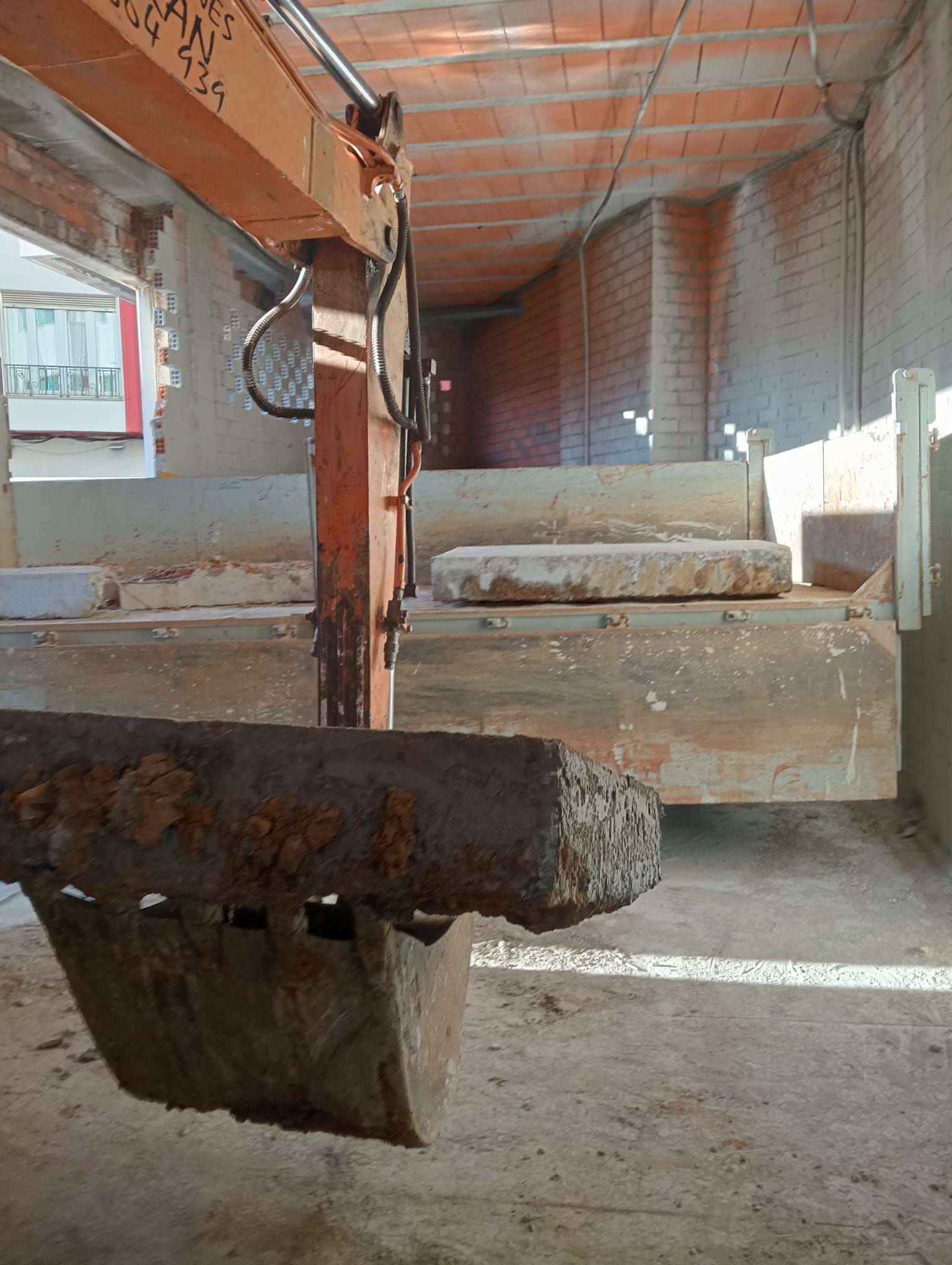 Una vieja pala excavadora dentro de un almacén con paredes de ladrillo y bloques de hormigón apilados.