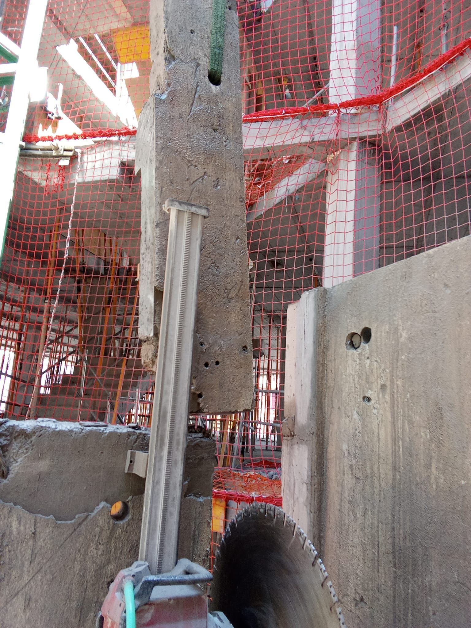 Obra en construcción con pilares de hormigón, redes de seguridad rojas y andamios de barras de refuerzo.