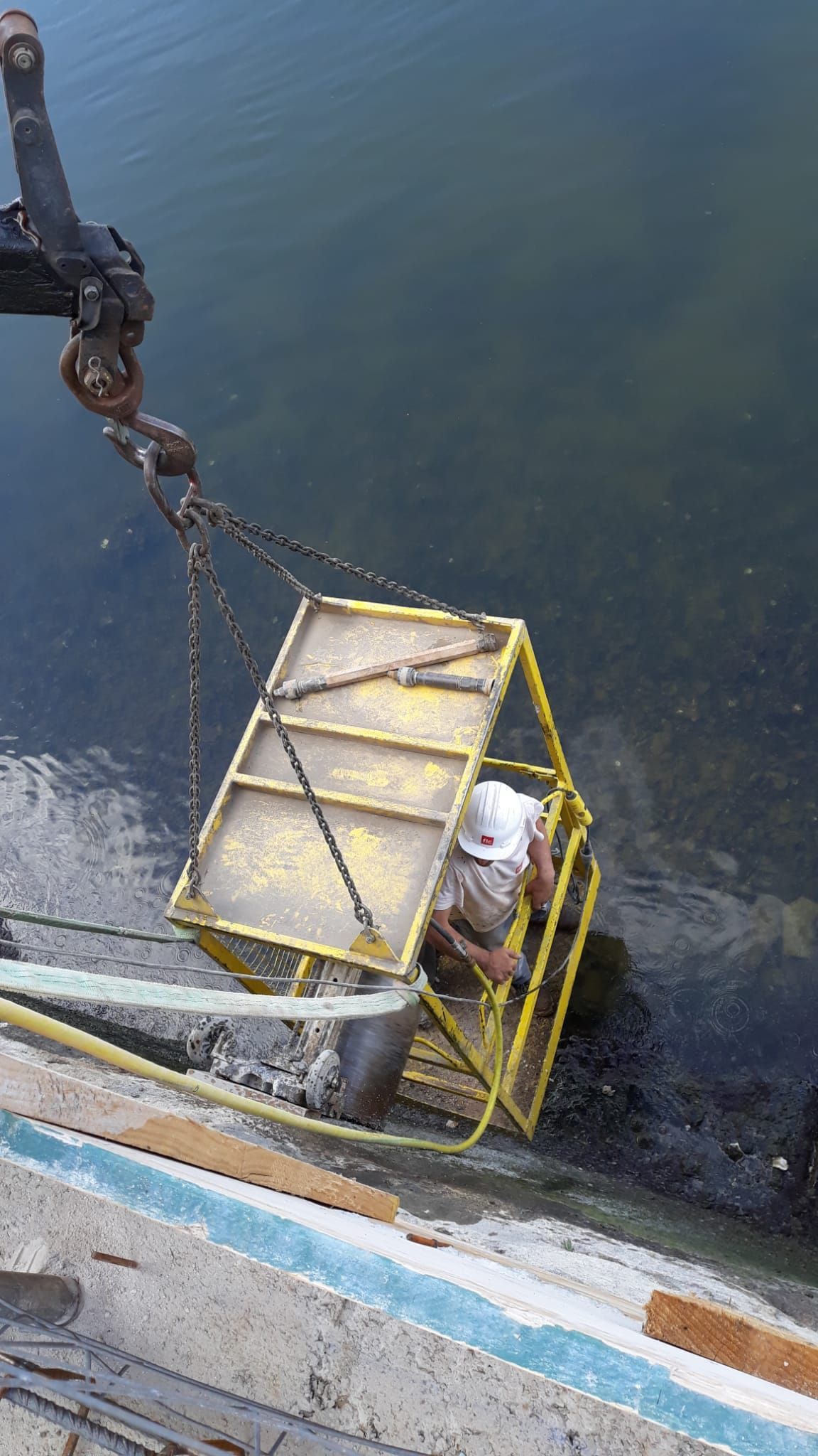 Un elevador de botes de jaula metálica amarilla baja una pequeña embarcación a aguas oscuras junto a un muelle.