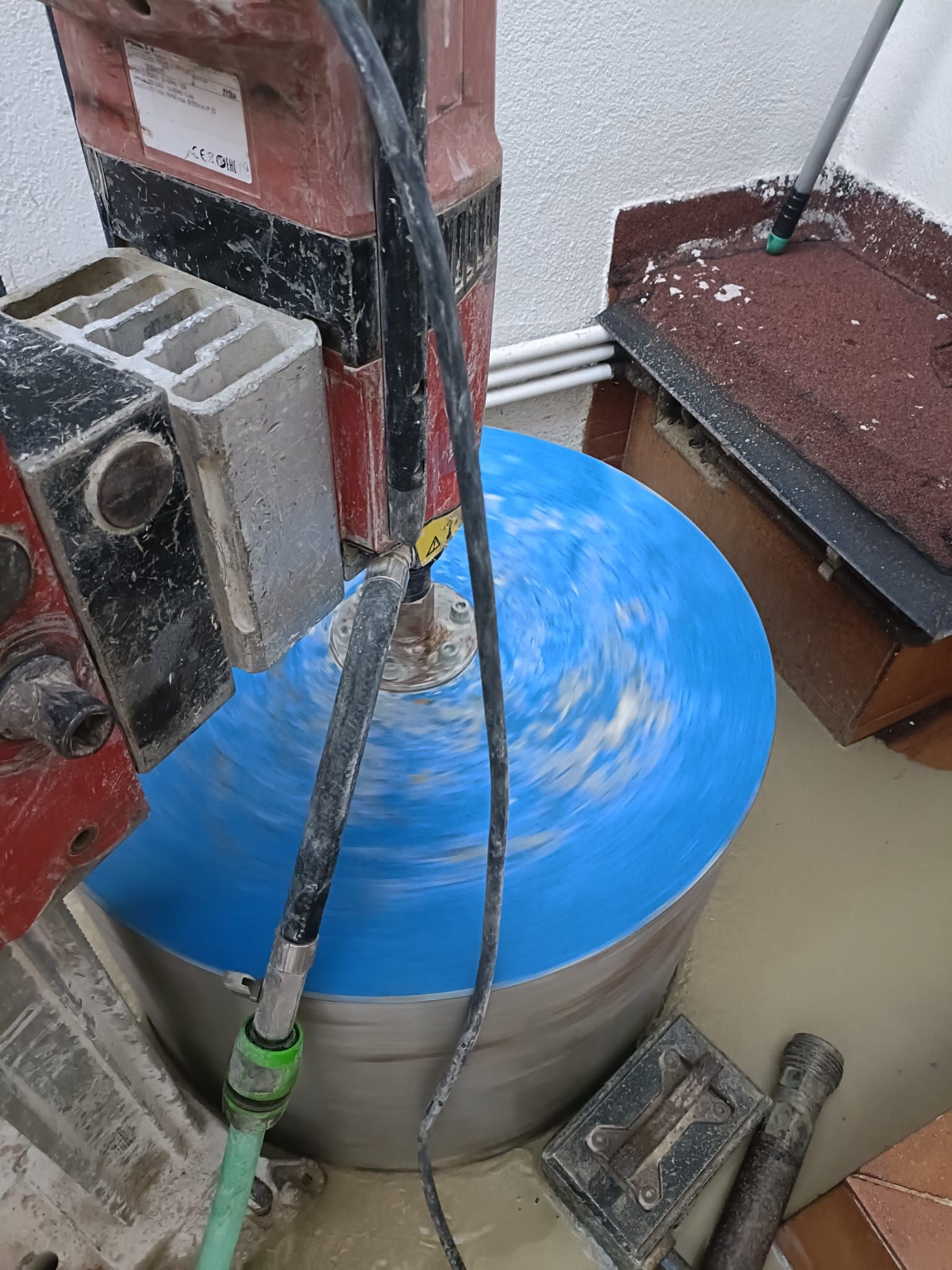 Tanque cubierto con una lona azul junto a maquinaria roja en una zona industrial húmeda.