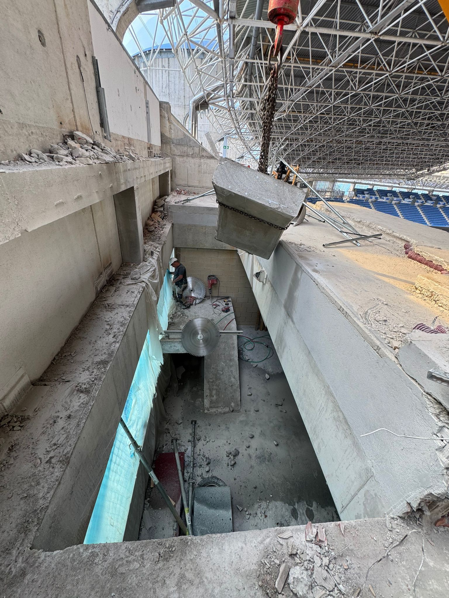 Daños en el interior de una zona de asientos del estadio, con hormigón derrumbado y estructura metálica expuesta en la parte superior.
