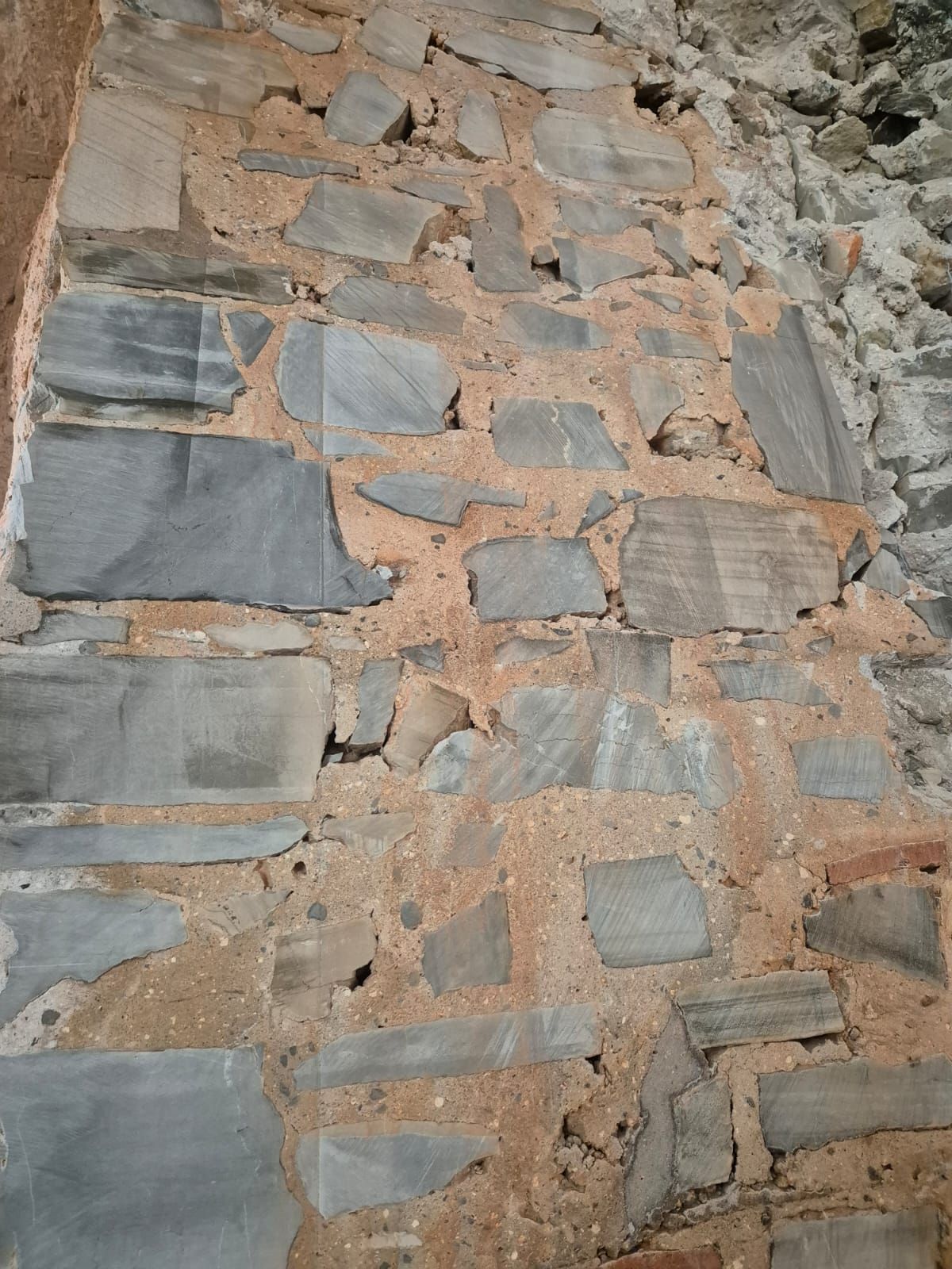 Primer plano de un muro de piedra tosca con parches de pizarra gris y mortero color canela.