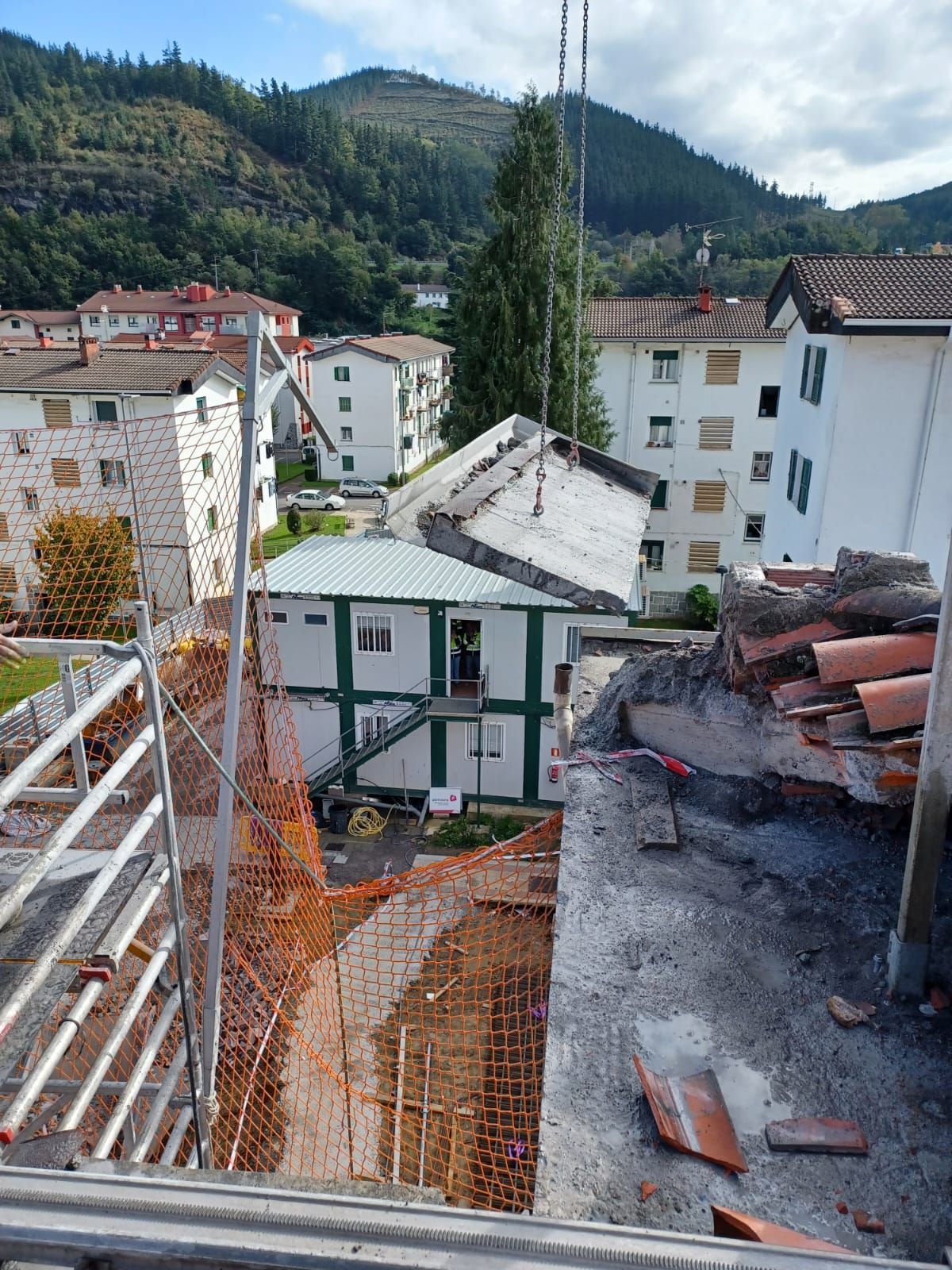 Obra en construcción en la azotea con vistas a las casas del pueblo y a las verdes colinas, con escombros y andamios en primer plano.